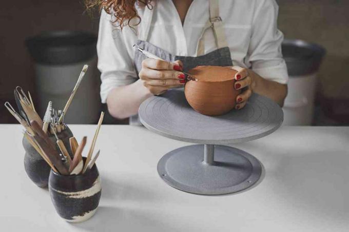 Bránice ženského hrnčíře tvarující tvar do hlíny s pracovním nástrojem u stolu