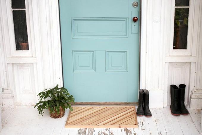 Açık mavi bir kapının önünde ahşap bir paspas.