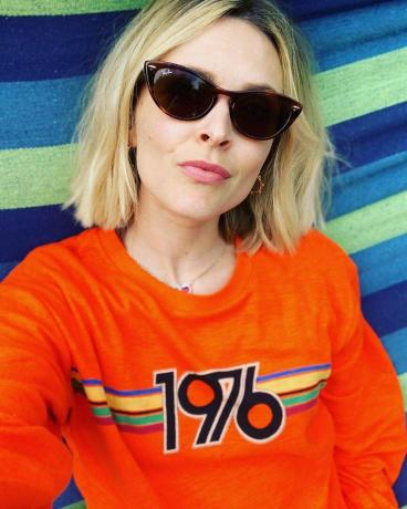 Fearne medvilniniai plaukai: Fearne dėvi oranžinį megztinį su akiniais nuo saulės