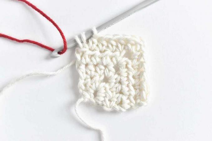 Um pedaço de fio vermelho sendo enganchado em uma agulha de crochê cinza