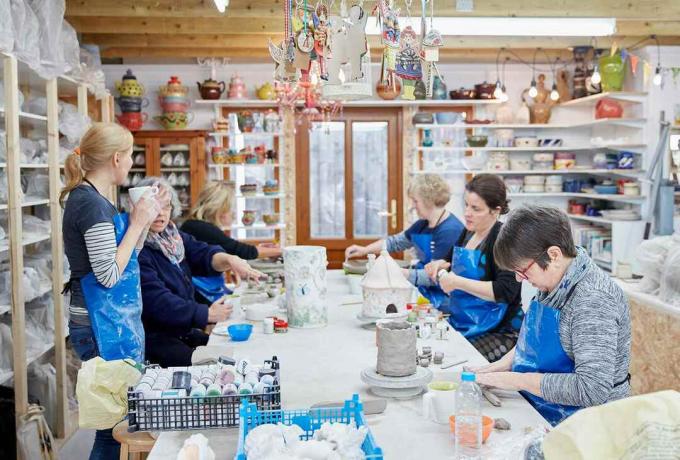 Skupina lidí sedí na pracovním stole v keramické dílně.