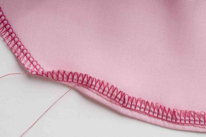 Ponto overloque e ponto reto ao longo da borda curva do tecido rosa