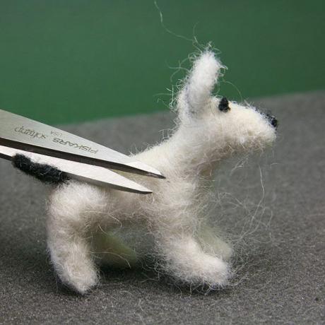 A tesoura corta as fibras soltas do corpo de um cão feltro com escamas de casa de bonecas.