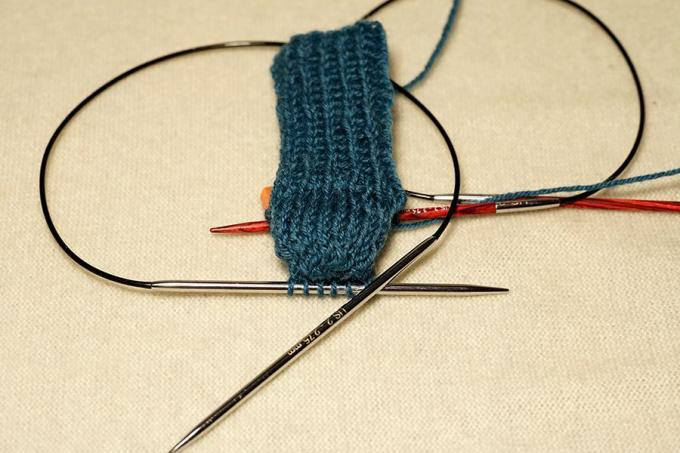 Оформен плетен син чорап с игли за свързване.