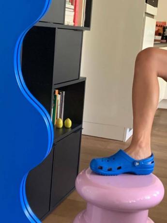 sepatu crocs: nicole huisman mengenakan crocs biru berdiri di bangku merah muda di cermin biru