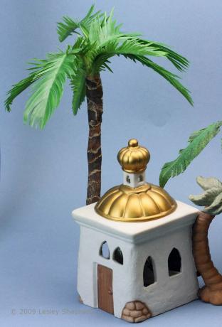 Skala miniaturowa palma ustawiona za porcelanowym budynkiem w szopce bożonarodzeniowej.